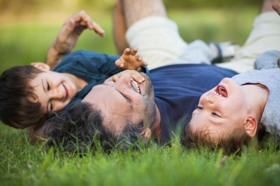 Father laying in the grass with two young children on Father's Day