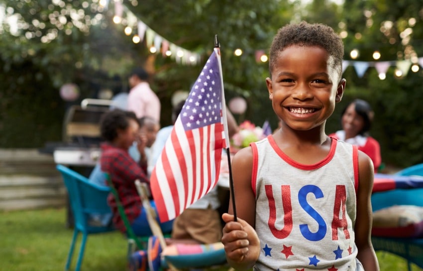 school-age child holding American flag as his family celebrates the 4th of July in their backyard