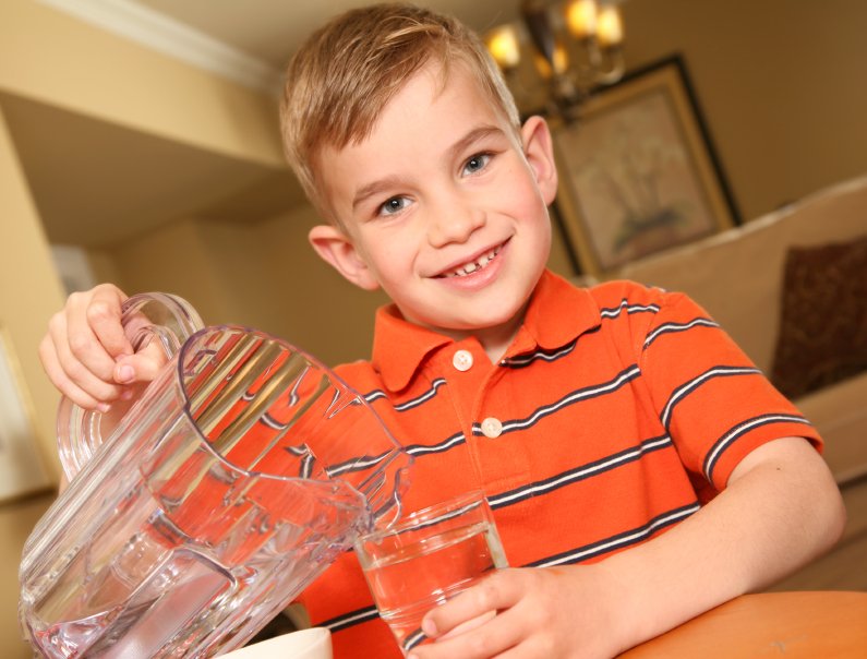school-age child pouring a glass of water to stay hydrated