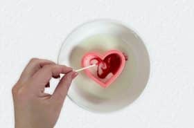 Hand stirring red food coloring within Valentine's Day cookie cutter placed in milk