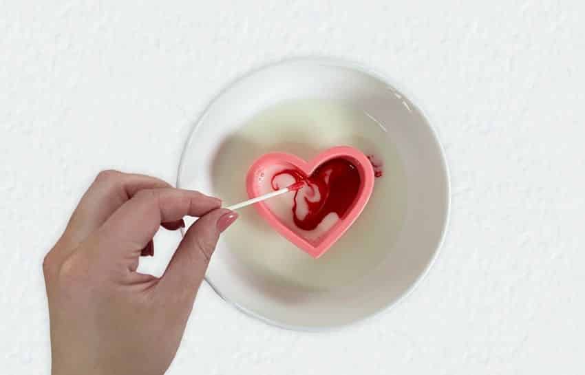 Hand stirring red food coloring within Valentine's Day cookie cutter placed in milk