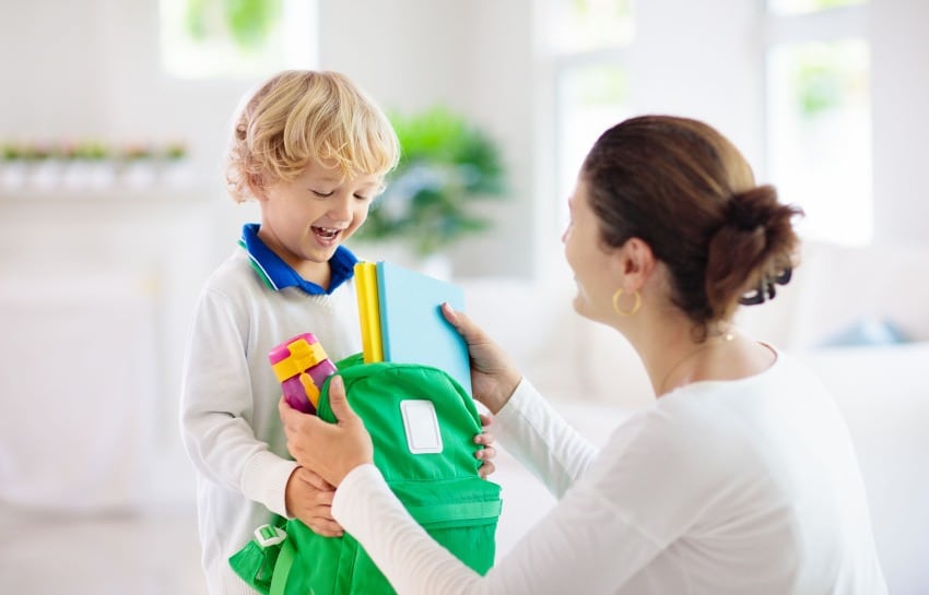 mother handing child backpack before school