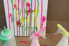 pink yellow and green paint splattered on a white canvas from spray painting art project