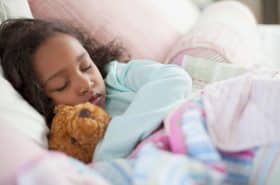 Child sleeping in bed with teddy bear