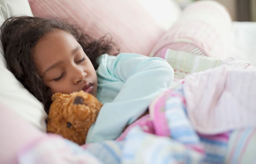 Child sleeping in bed with teddy bear