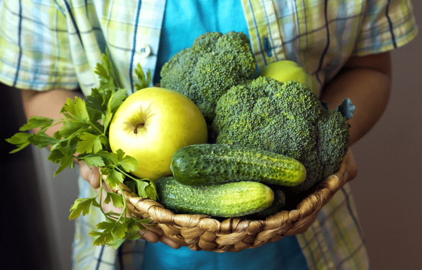 child holding bowl of green fruits and green vegetables