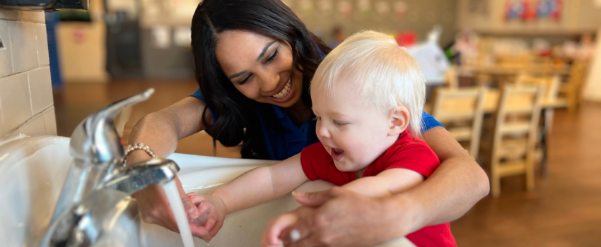 Teacher helping child wash his hands at daycare to practice healthy habits