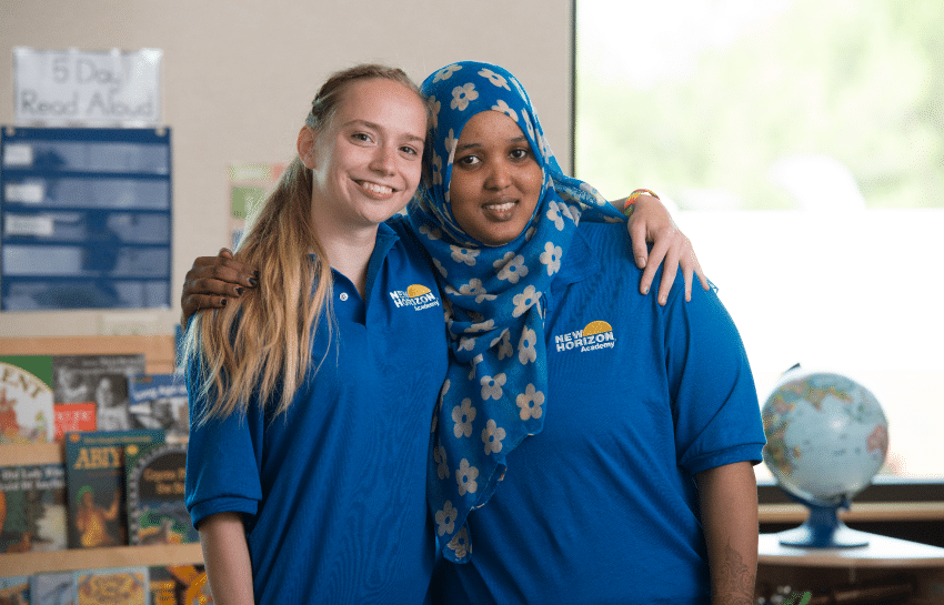 Two New Horizon Academy childcare teachers smiling and hugging while working in a classroom