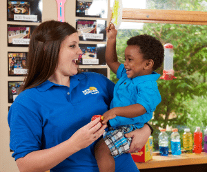 Daycare teacher smiling holding toddler at school