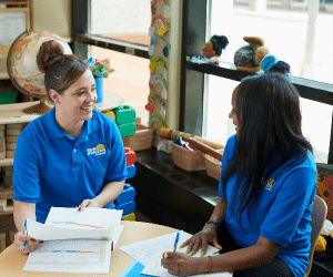 Daycare teachers helping each other with paperwork while conversing