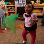 Toddler girl playing the ribbon dance in her classroom at New Horizon Academy