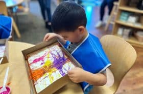 Preschool child rolling marble across painted paper to make marble painting art