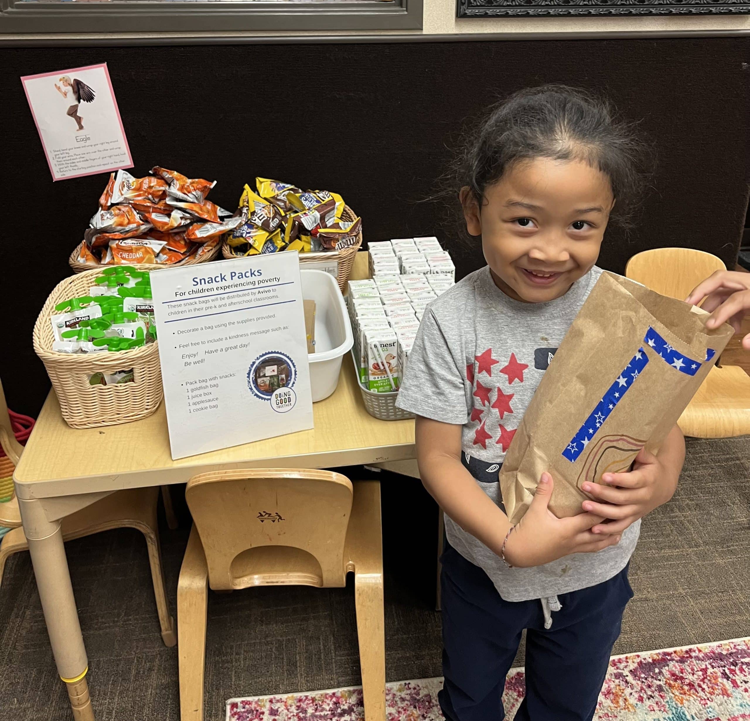 New Horizon Academy child holding a snack pack they put together for Doing Good Together's Family Service Event