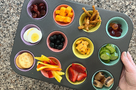 muffin tin charcuterie boards for kids including snacks such as grapes, cheese, eggs, blueberries, goldfish crackers, bell peppers, strawberries, cucumbers, and more