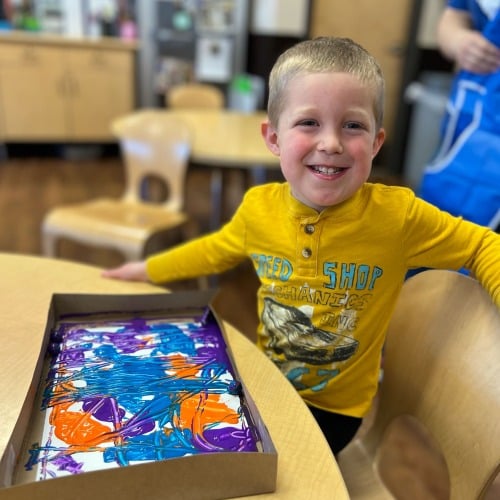 preschool boy smiling with his finished marble painting craft art at New Horizon Academy daycare