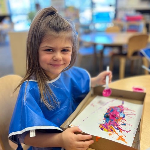 preschool girl smiling with her finished marble painting craft art at New Horizon Academy daycare