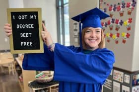 New Horizon Academy teacher graduating from debt-free degree scholarship program, holding a sign that says "I got my degree debt-free"