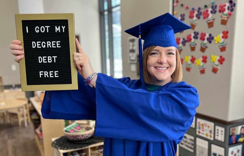 New Horizon Academy teacher graduating from debt-free degree scholarship program, holding a sign that says "I got my degree debt-free"