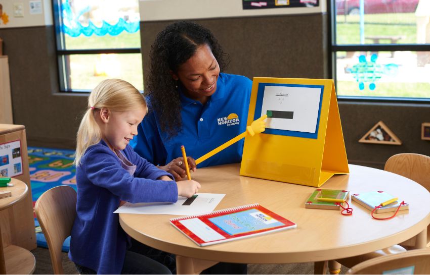 Teacher helping child with their writing skills in New Horizon Academy's preschool program