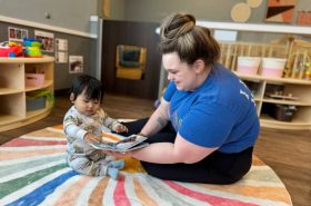 Infant daycare teacher reading a hardcover book to baby