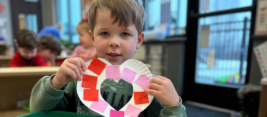 Preschool child holding completed Valentine's Day heart wreath craft