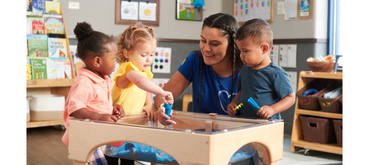 http://Teacher%20playing%20with%20toddler%20children%20around%20an%20interactive%20sensory%20table