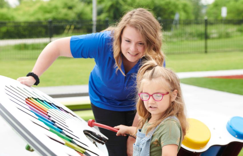Preschool teacher and child engaged in an outdoor musical learning activity as part of New Horizon Academy's summer program